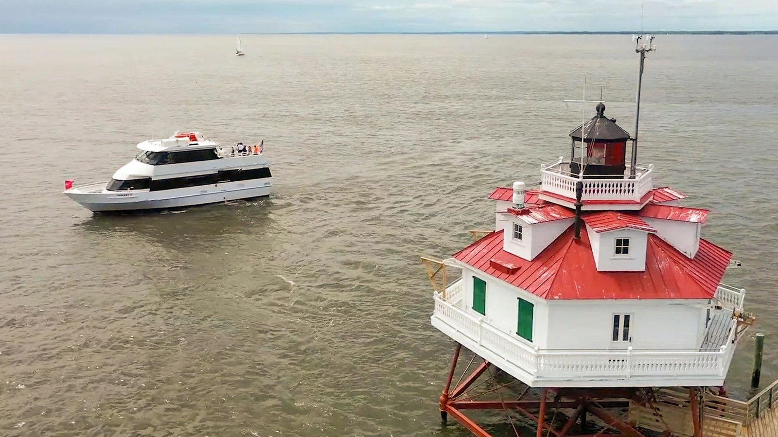 Tour boat near the Thomas Point Shoal Lighthouse with a red roof. Cloudy sky and calm water.
