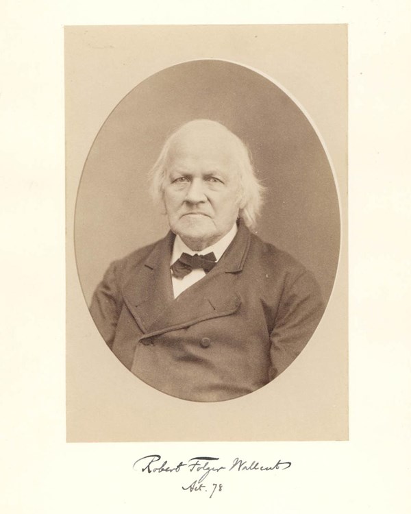 An old white man with thin white hair wearing a black bow-tie, white collared shirt, and a dark coat