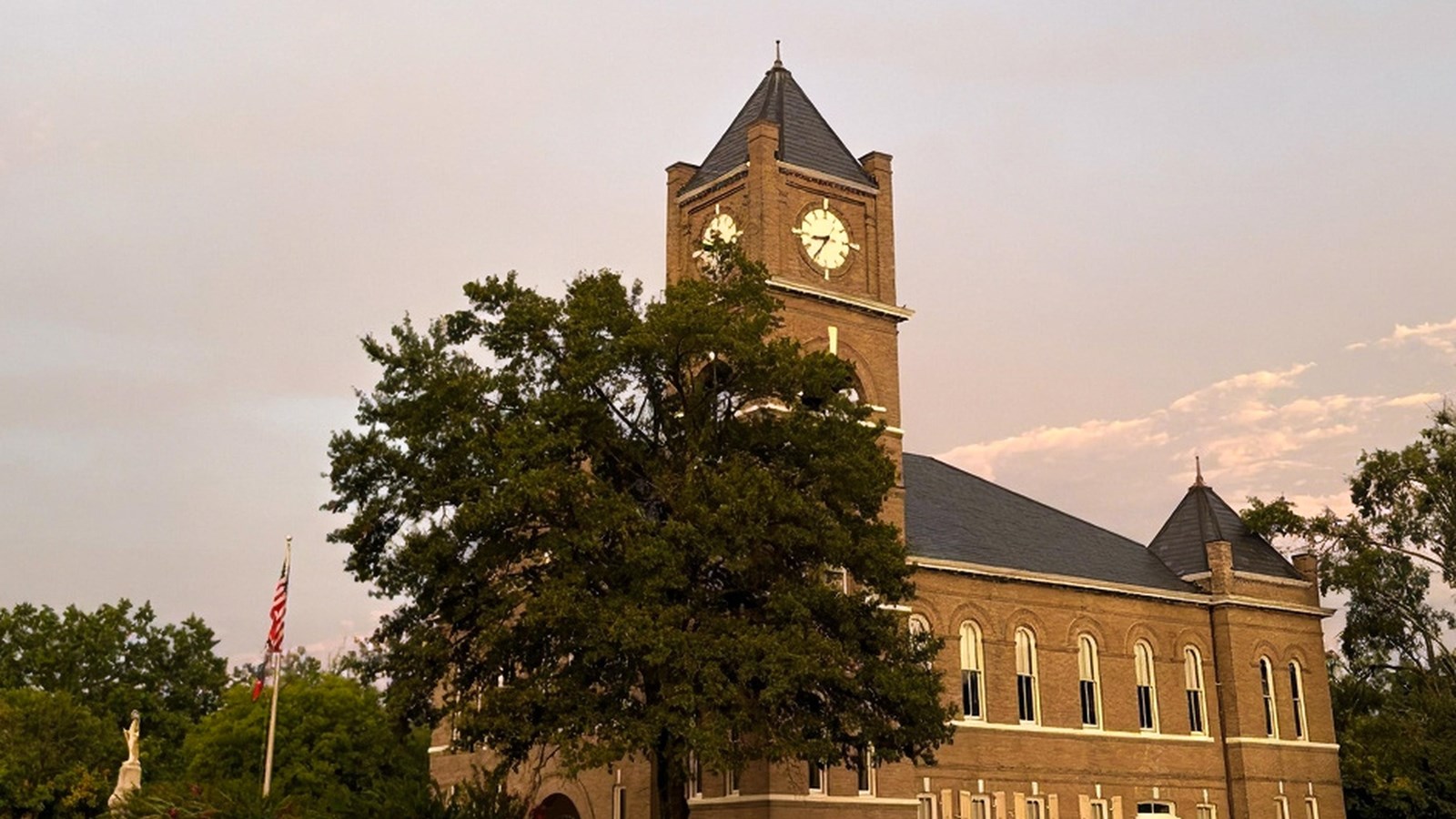 Front of a two-story brick courthouse with a clock tower. A tree stands in front. 