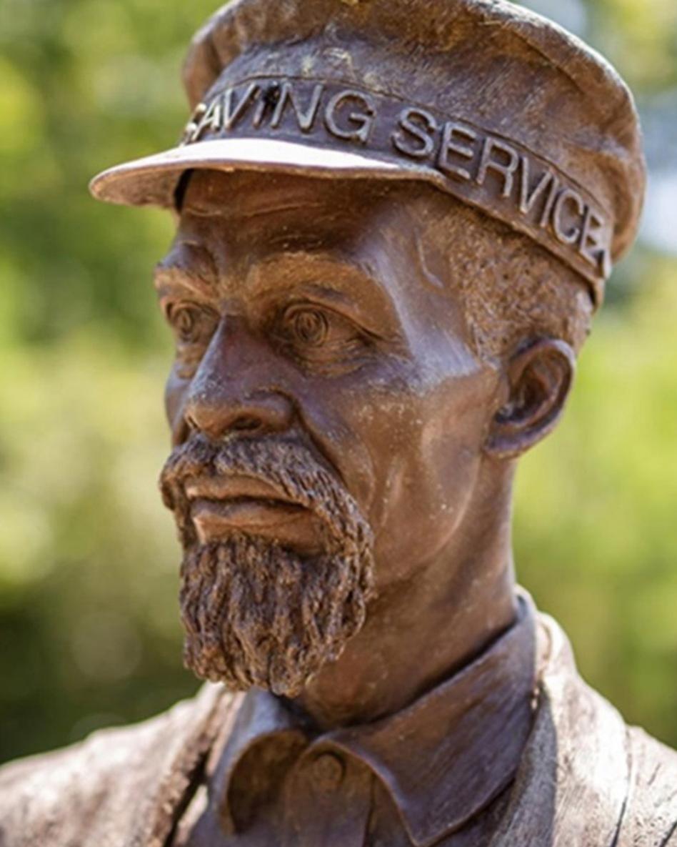 A bronze statue of a man shown from the shoulders up with a goatee and a hat reading Saving Service