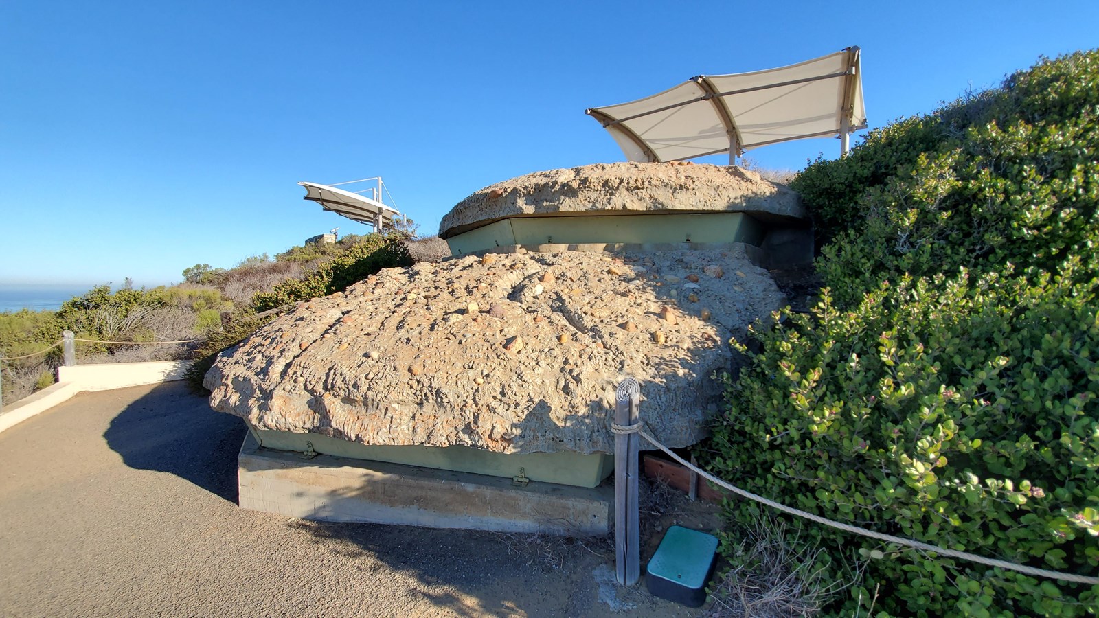 Structured made from two rounded, sandy-colored sections rises from a dusty-colored asphalt path.