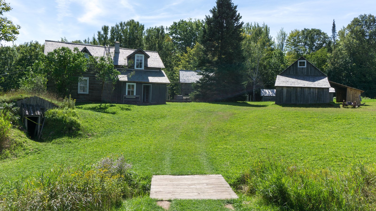 Summer scene of historic wooden home and out-buildings surrounded by trees.