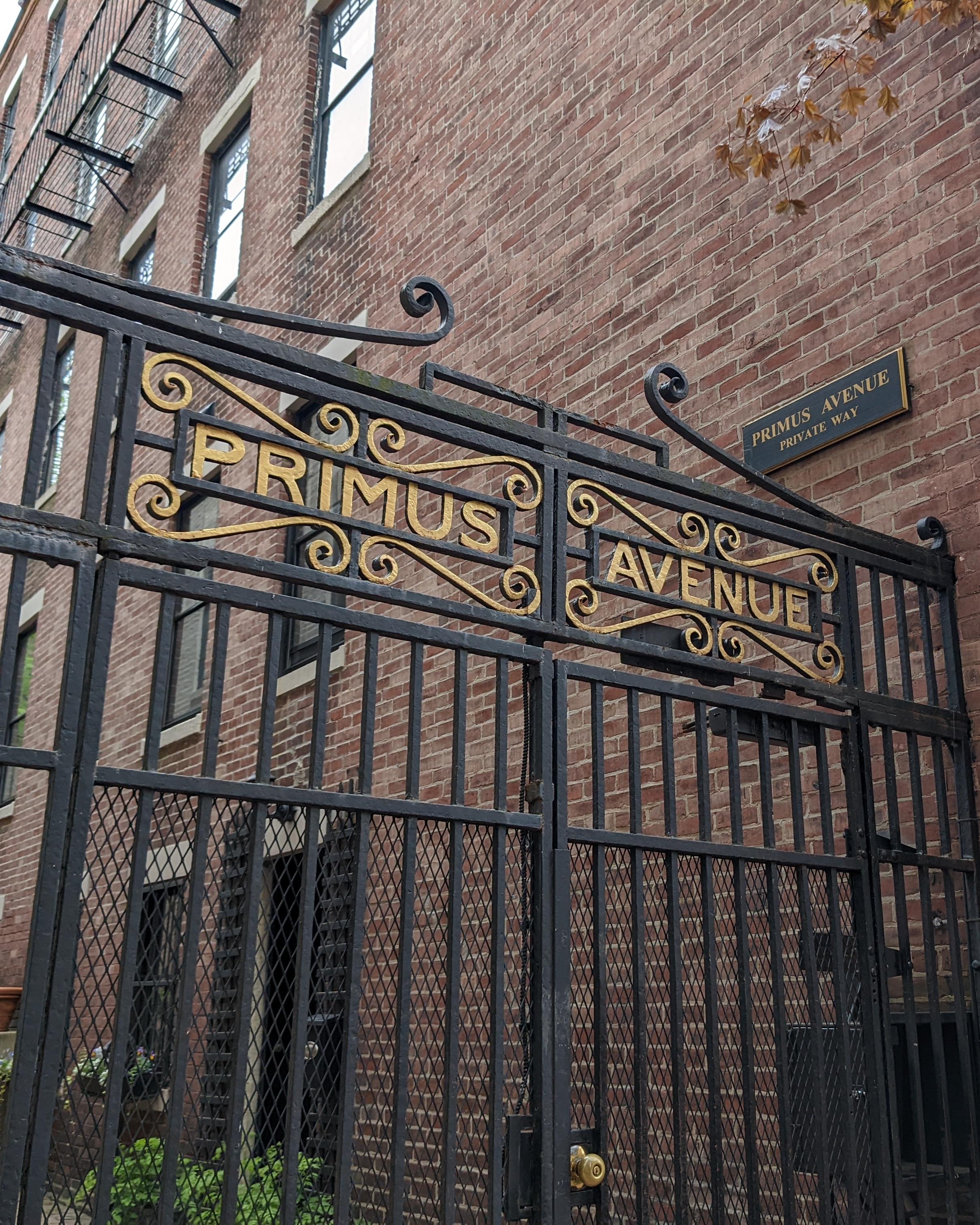 a black iron gate with the words primus avenue sits at the entrance of an brick lined alley