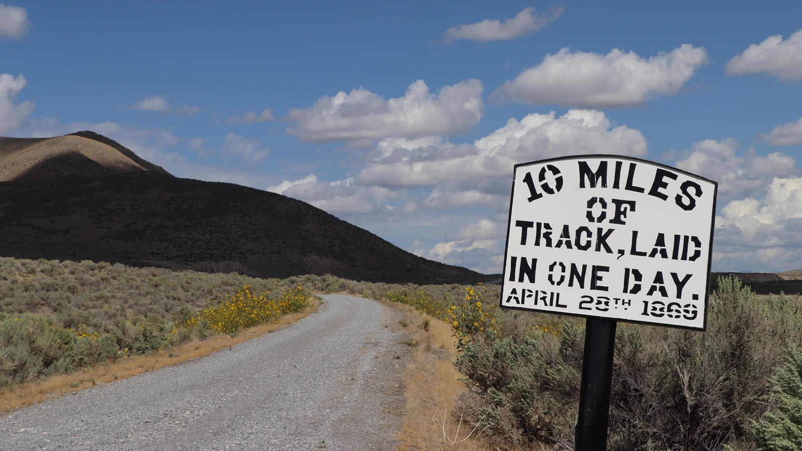 Gravel road through green, yellow and brown sagebrush landscapes, Historical sign on side of road