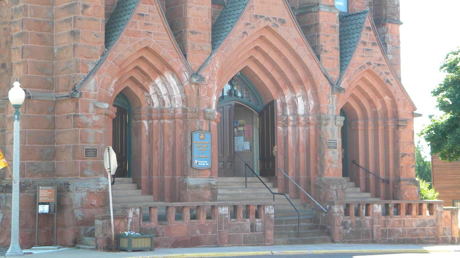 Summer scene of main entrance to red sandstone church.