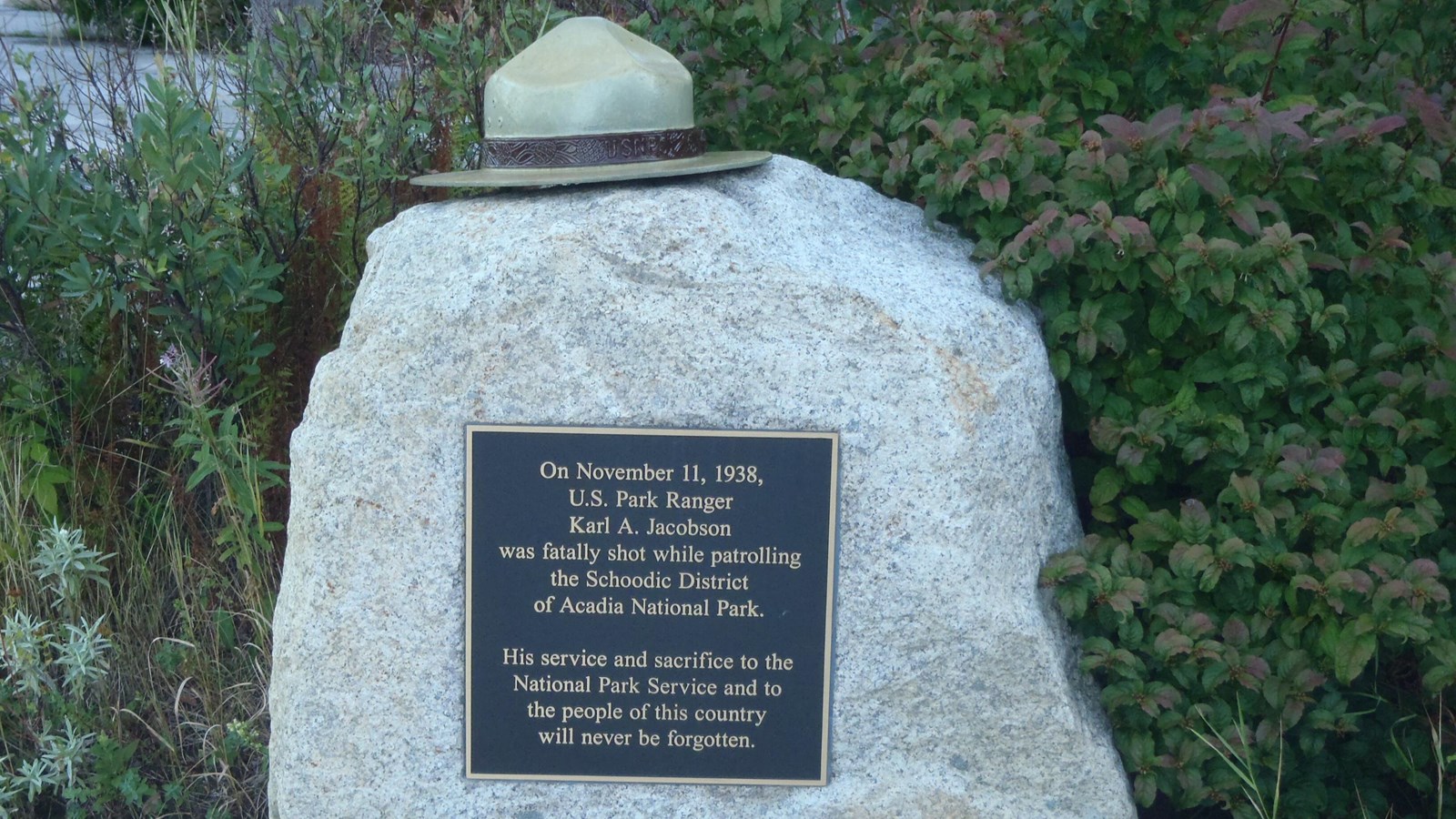 Bronze memorial plaque and ranger hat on a rock surrounded by cobblestones