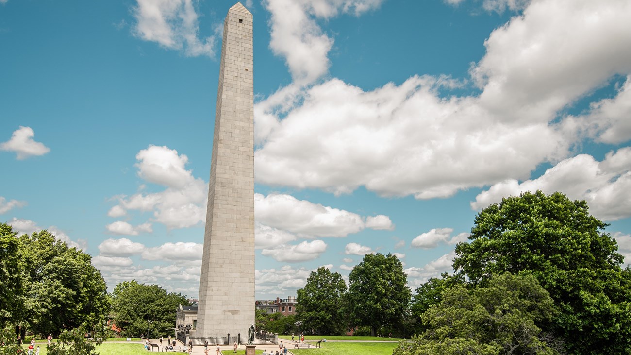 The tall obelisk monument stands under a bright blue sky in the middle of curated grassy grounds