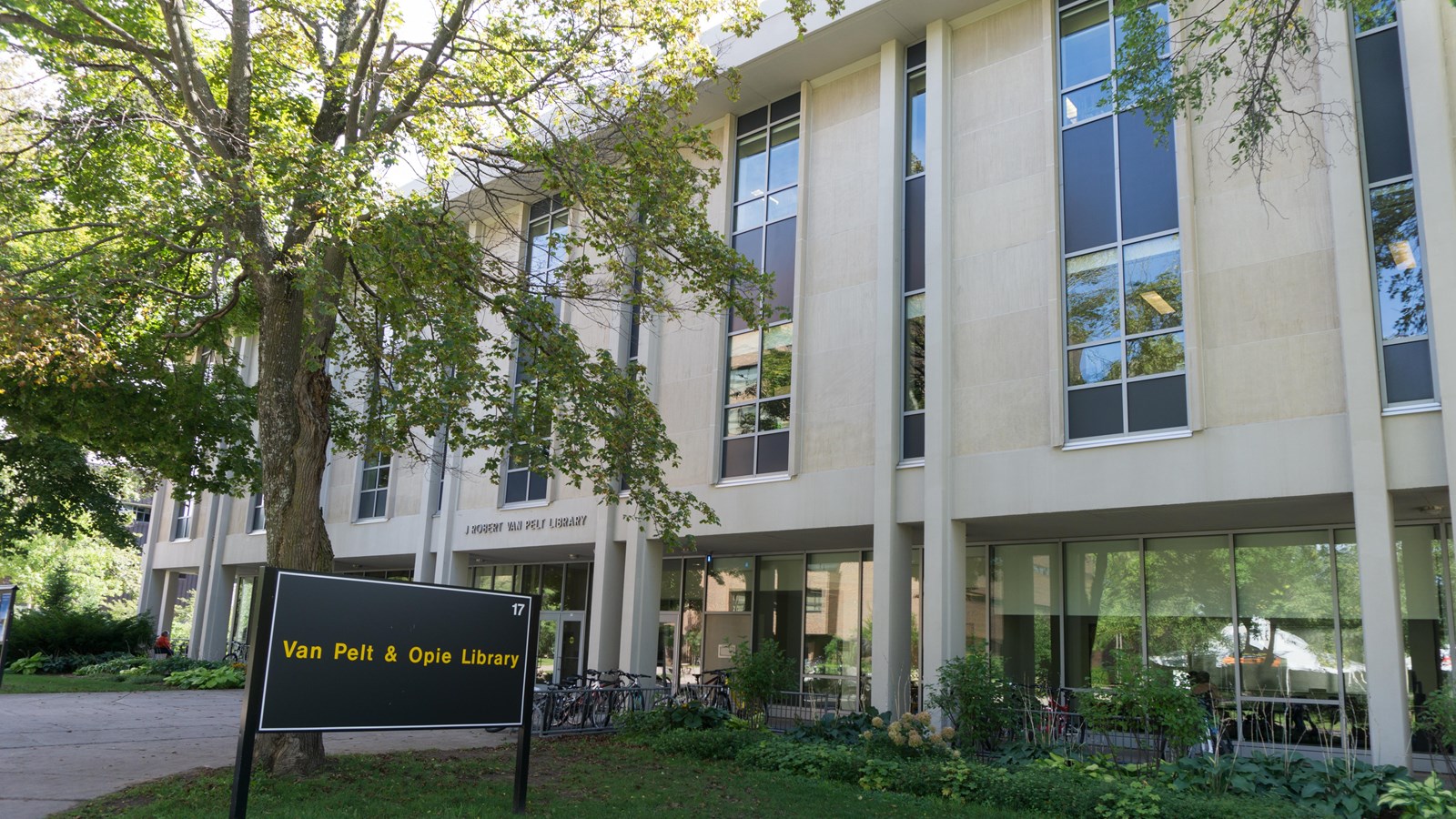 Summer scene of modern-styled concrete and glass building. Sign reads “Van Pelt and Opie Library.