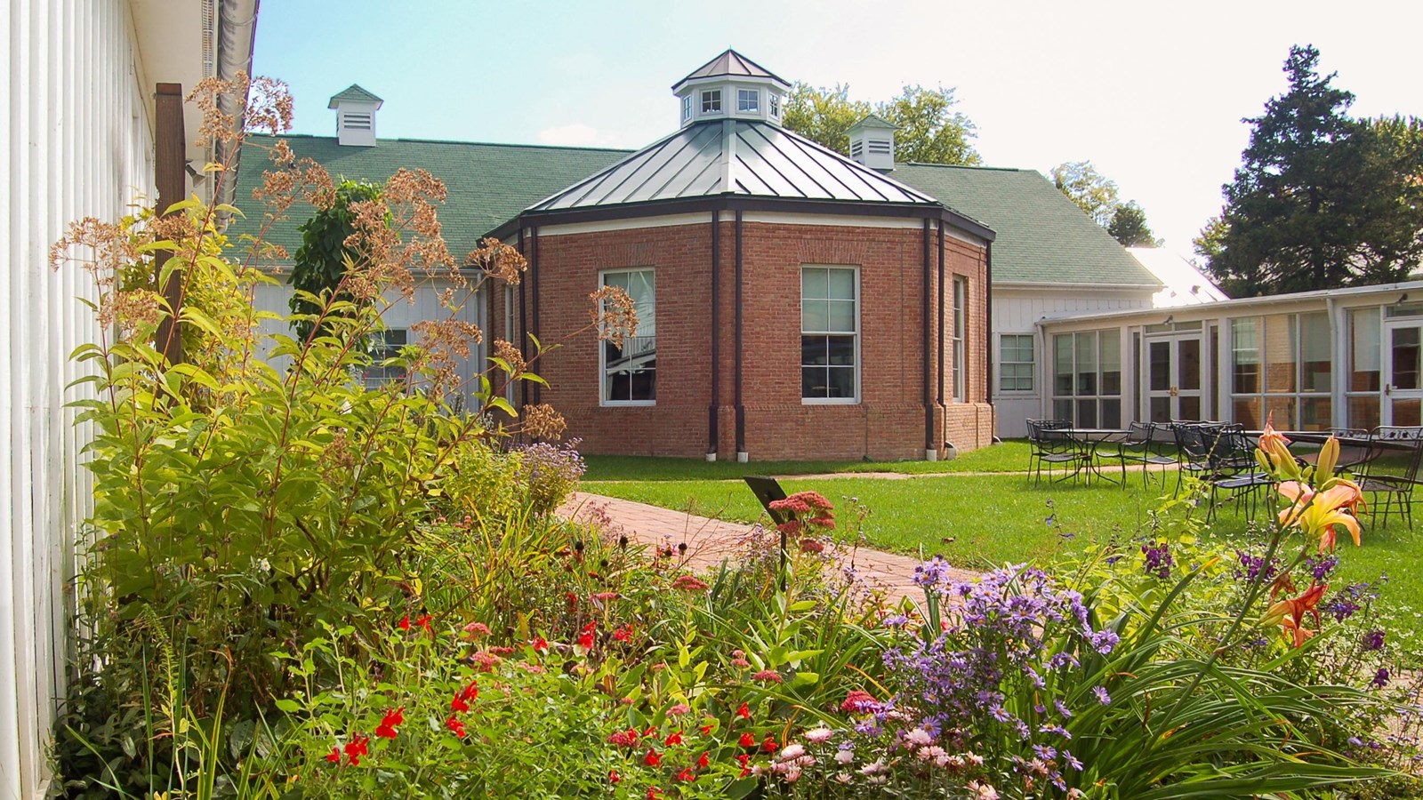 Sandy Spring Museum’s garden, library, and red brick building with flowers and a metal roof.