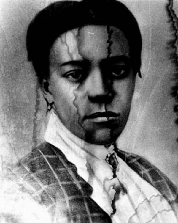 Black and white photo of Black woman from shoulders up in checkered dress. Photo has water damage.