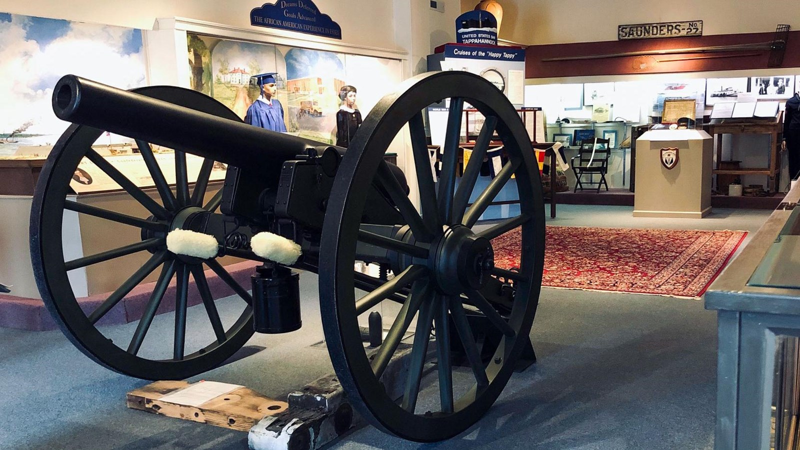 A museum exhibit featuring a large black cannon on wooden wheels, historical mannequins, and various