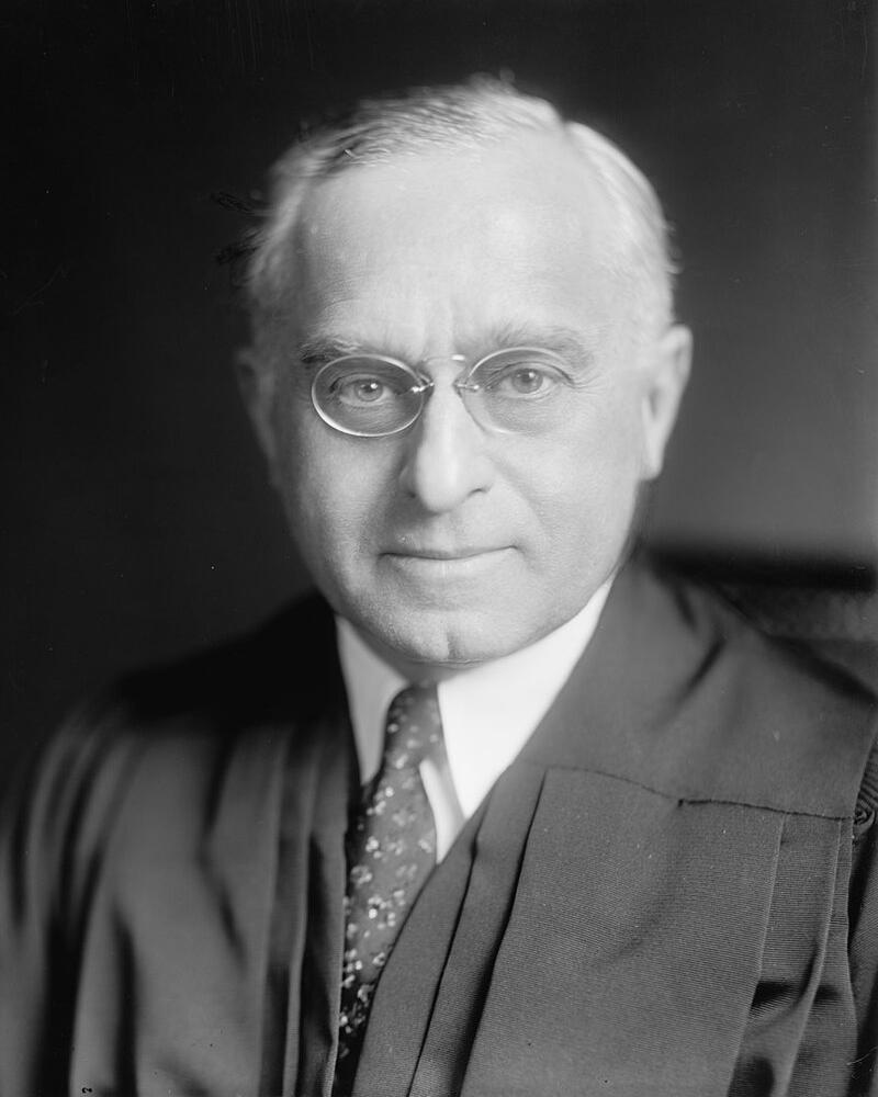Older white man with round glasses in black robes