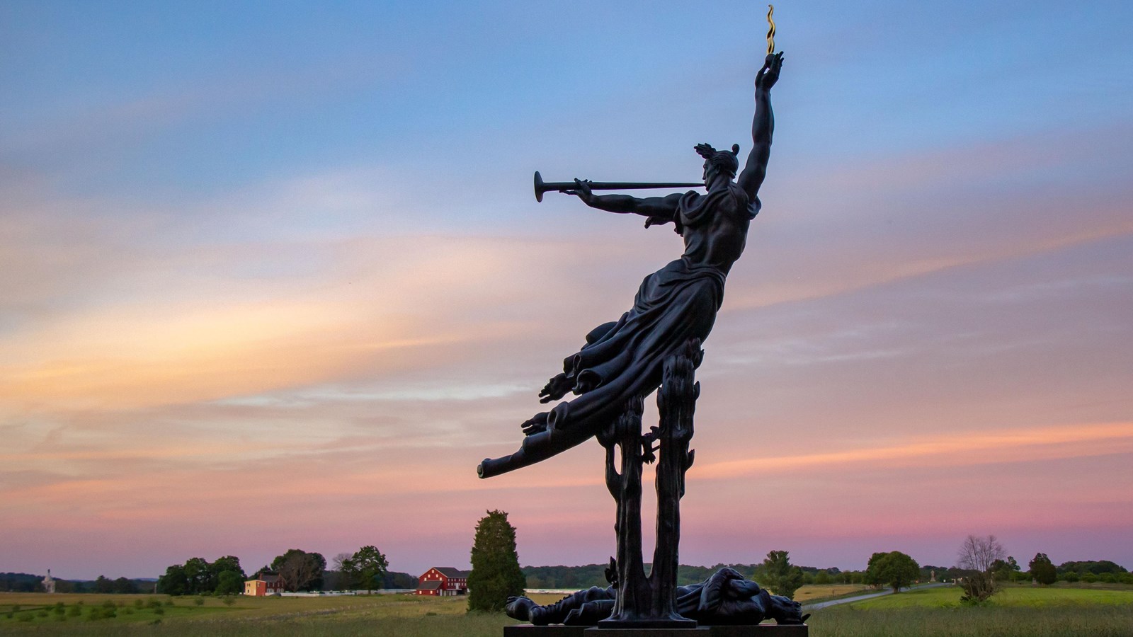 A bronze monument overlooking farm fields at sunset