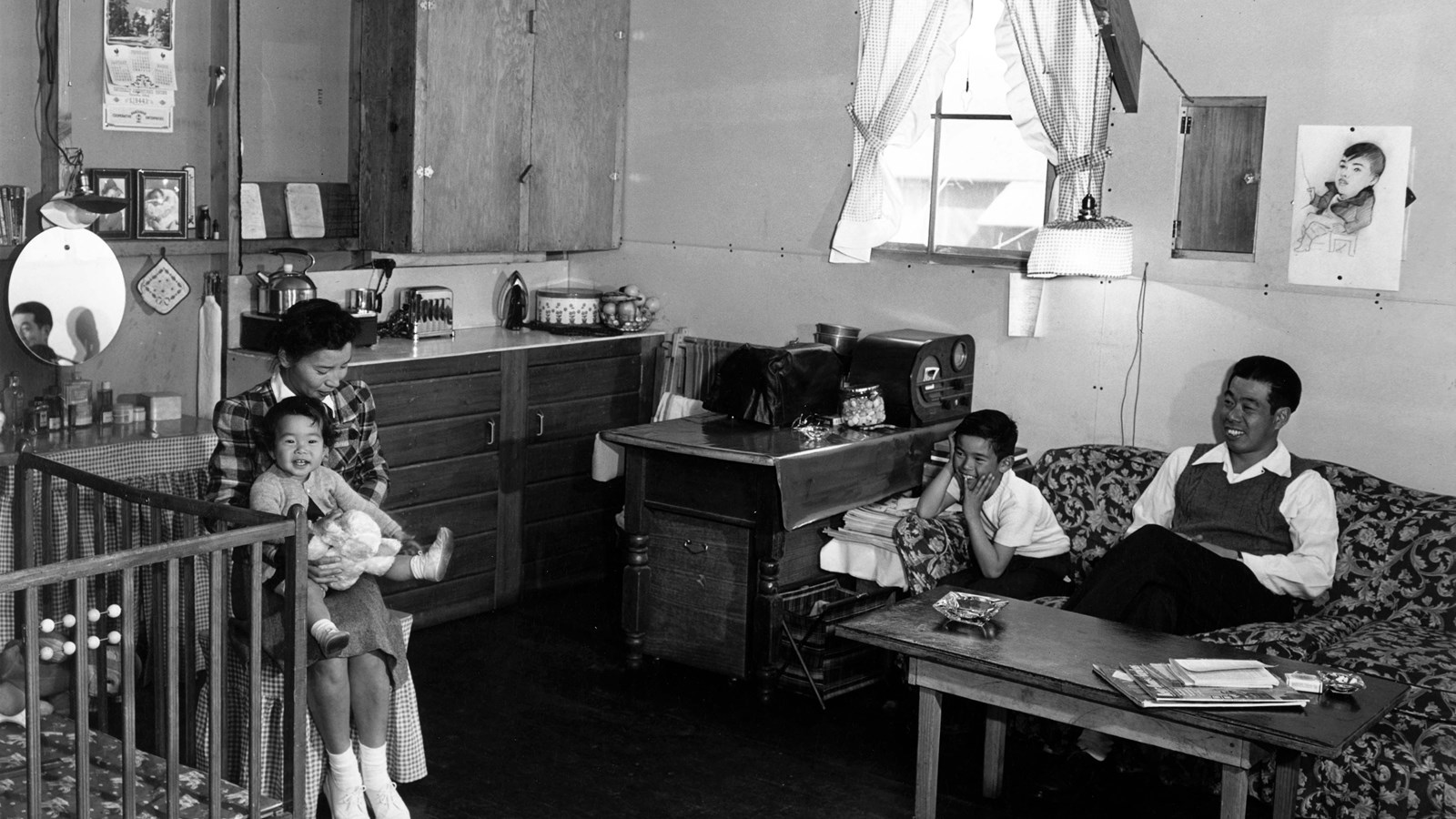 Small room with father and son on couch and mother and daughter next to crib.