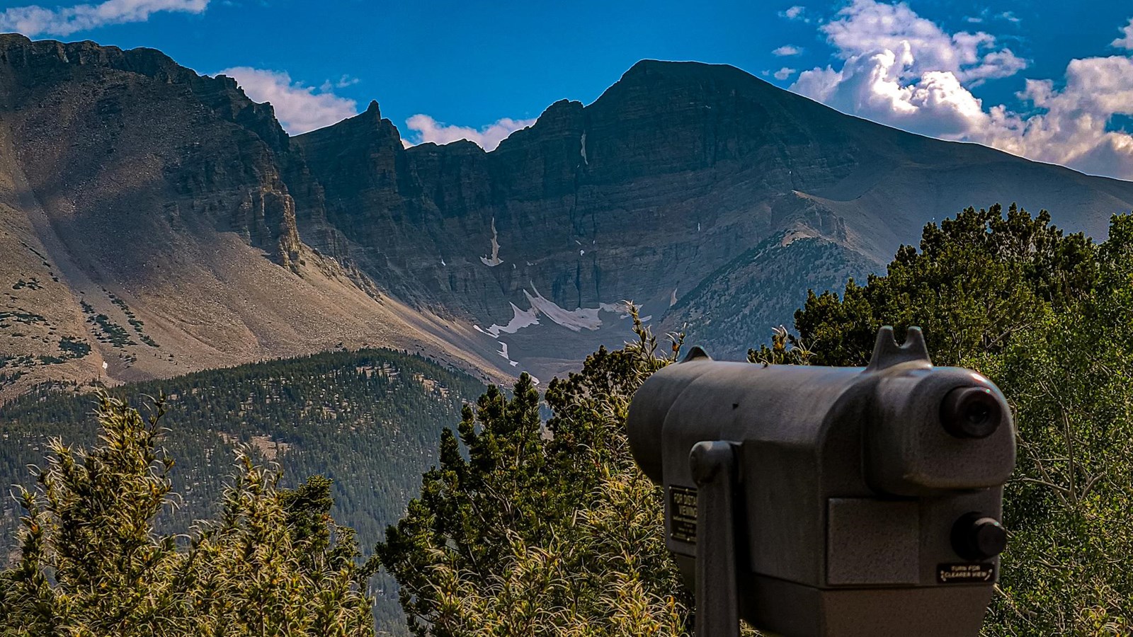 A grey viewing scope in the foreground. Beyond is Wheeler Peak with little snow left and blue skies.