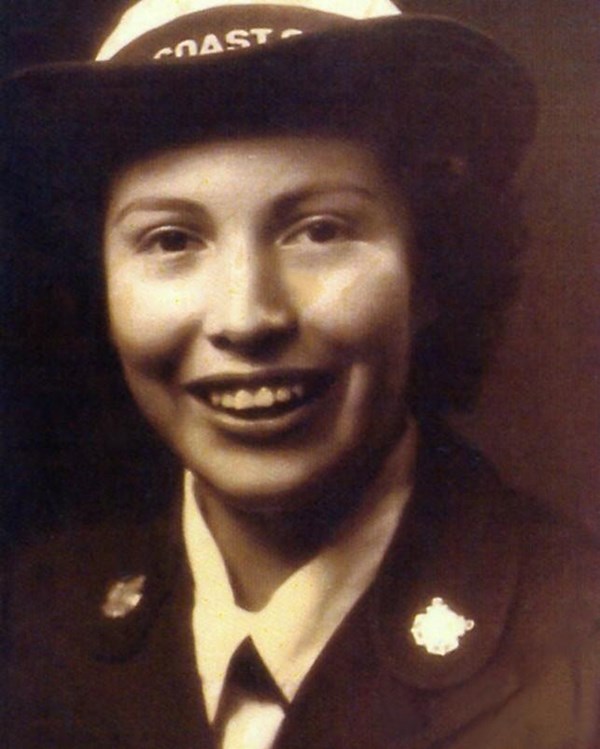 Young woman in coast guard uniform, shown by jacket pins and cap, smiles at the camera.