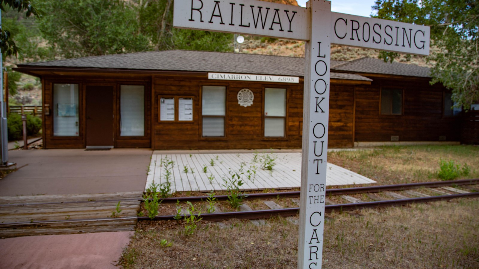 A railroad crossing sign in front of the tracks, with a small red building behind.