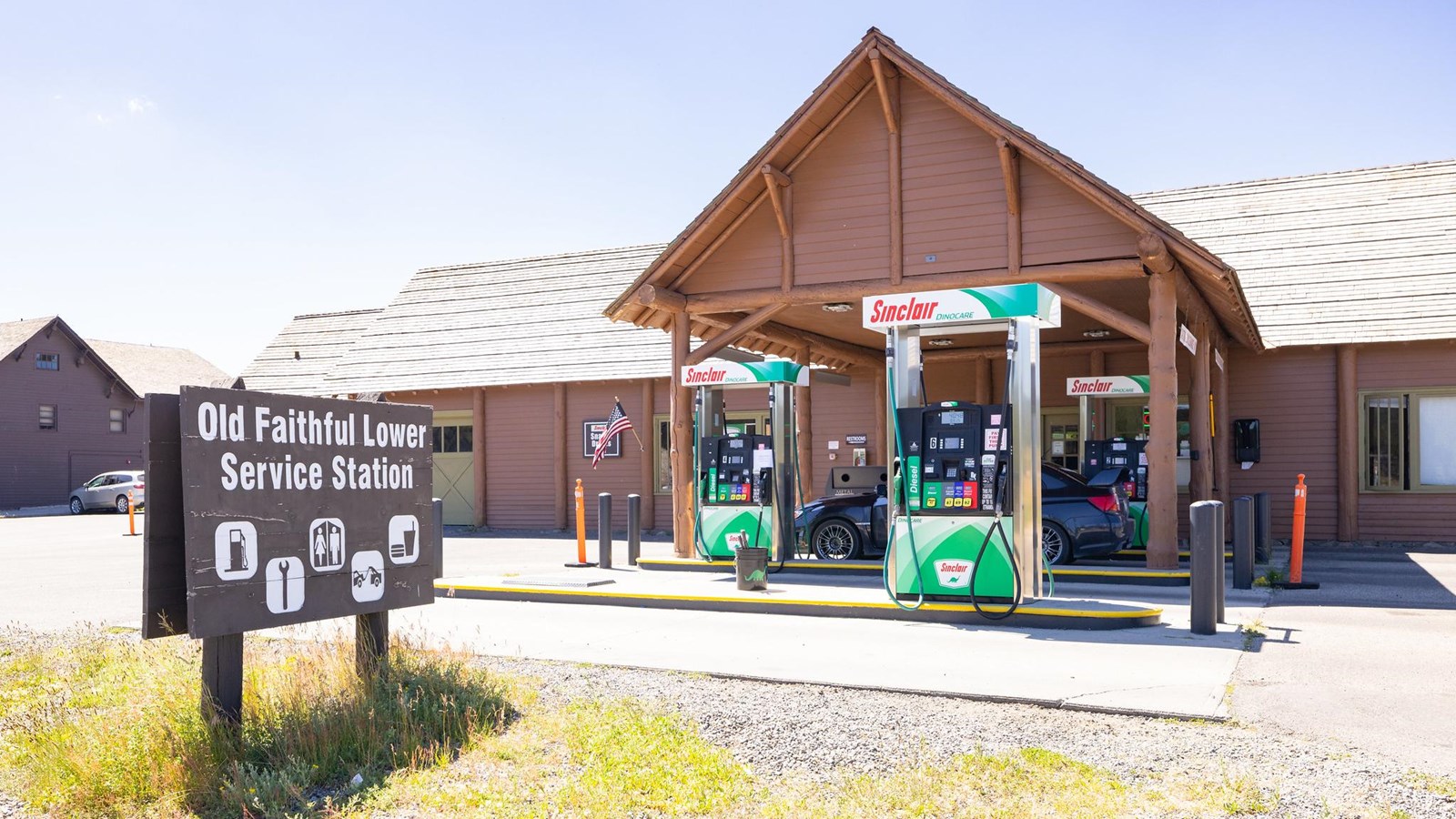 Four gas pumps sit underneath the protective roof of a brown building with siding.