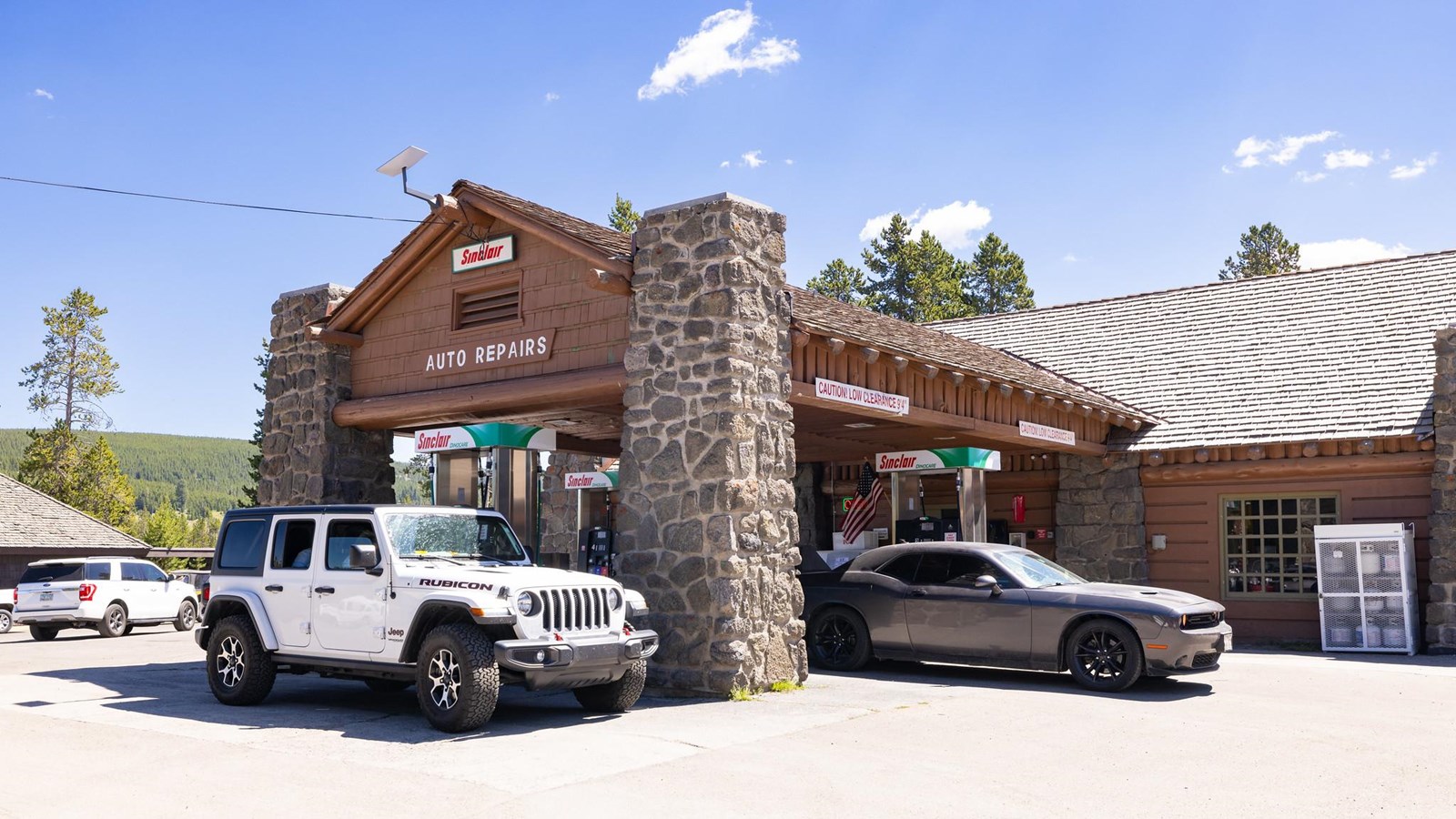 Four gas pumps sit underneath the protective roof of a brown building with siding and stone columns.