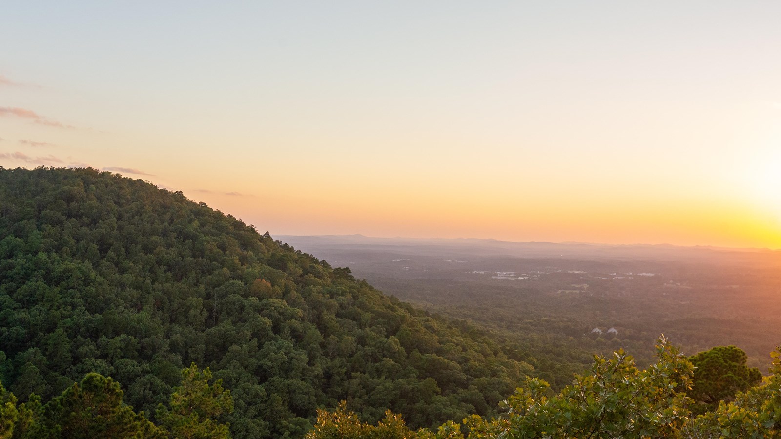 A sunset over a round hill spilling into a valley 