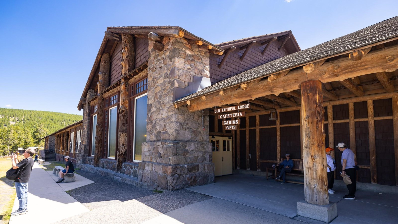 A building with wooden support beams, shingle siding, stone columns, and large windows.