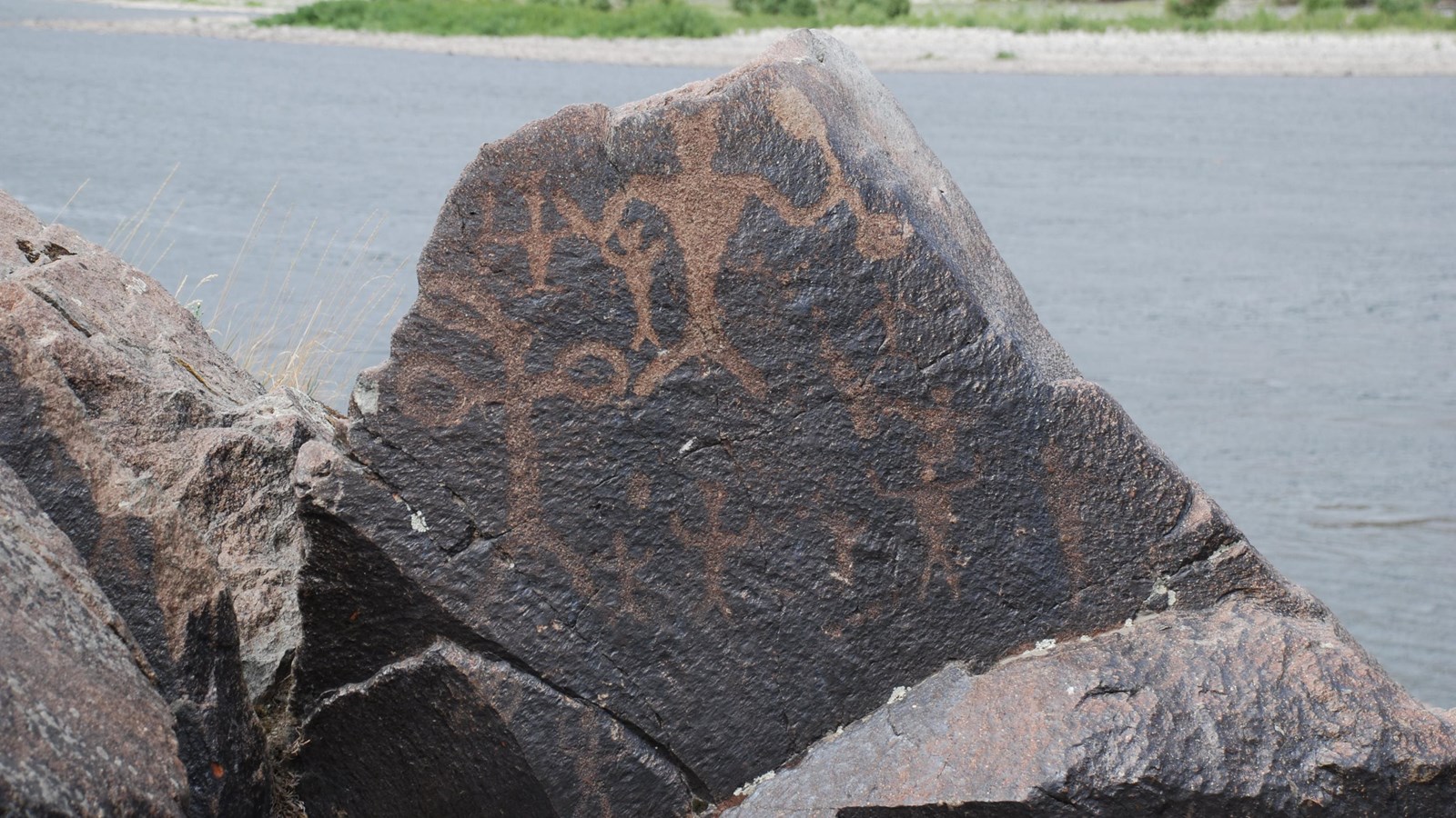 The rock carvings at Buffalo Eddy show up as lighter indentations on a dark basalt rock background