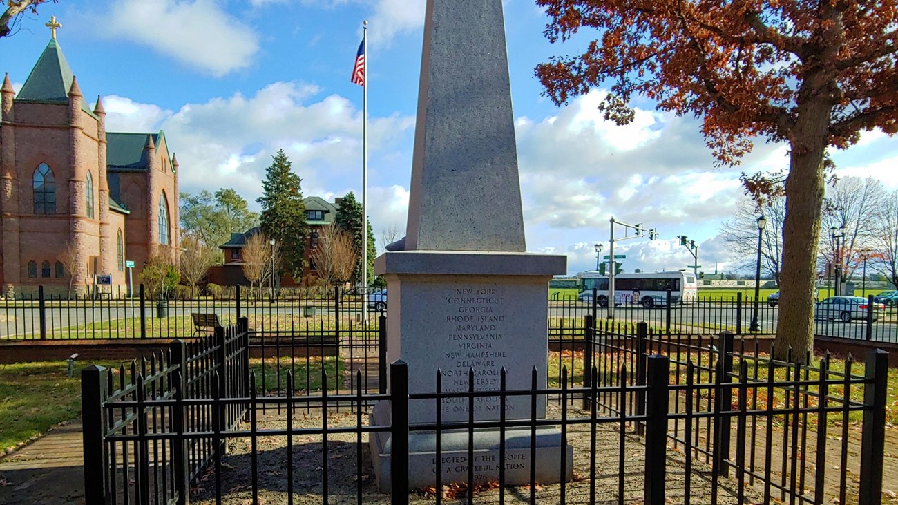 A view of a 20 foot tall, granite obelisk. It has words etched into the back. 
