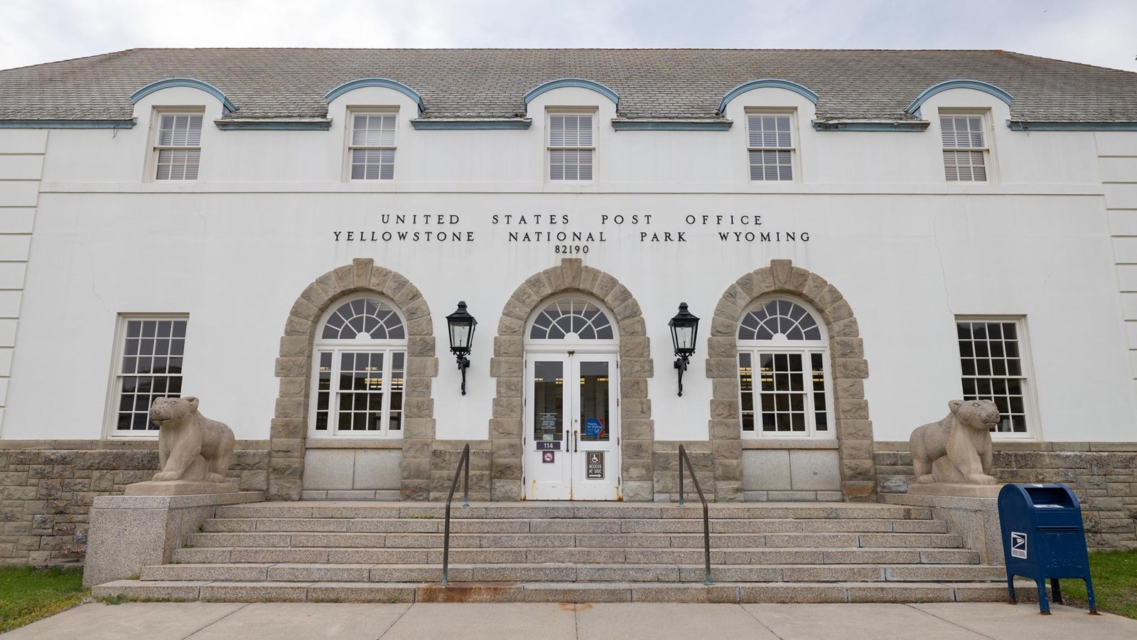 A concrete building with stone arches around the doors and a post office collection box in front.