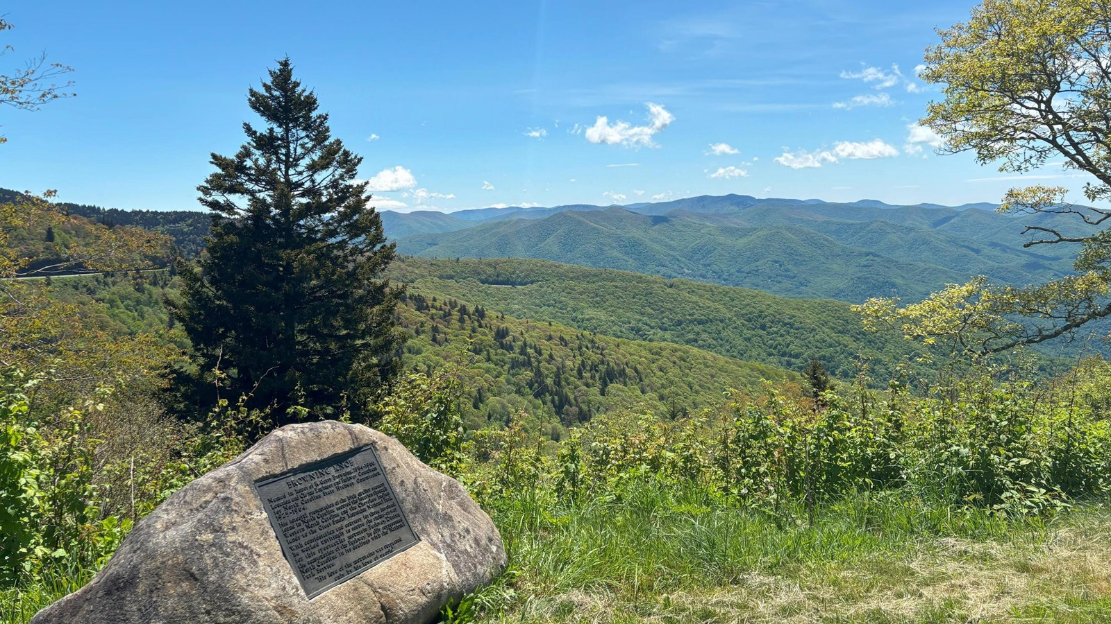 View of scenery with multiple mountain ranges. Historical marker on boulder in foreground