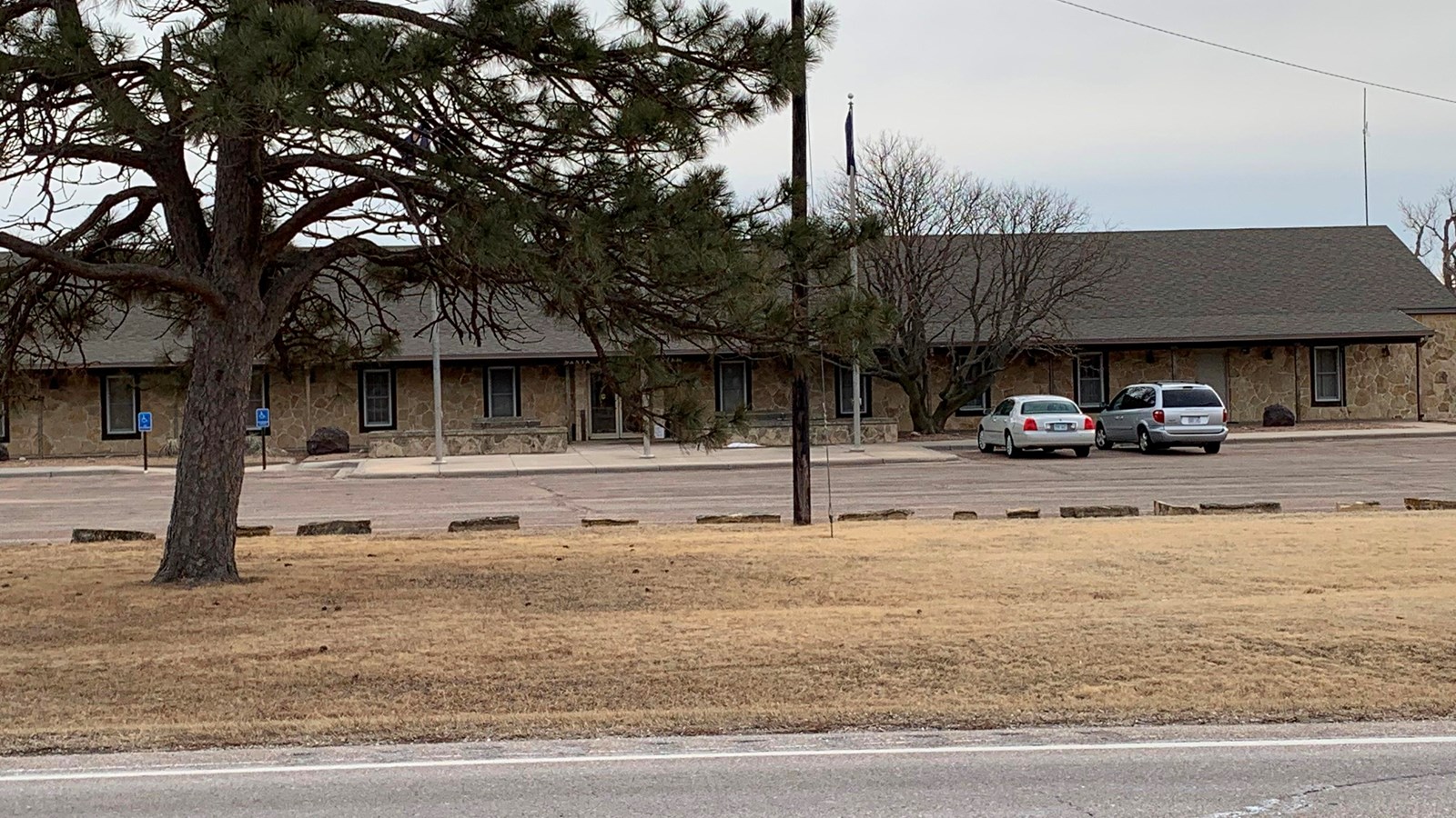 Sandstone building viewed from across a road with a parking lot in front.