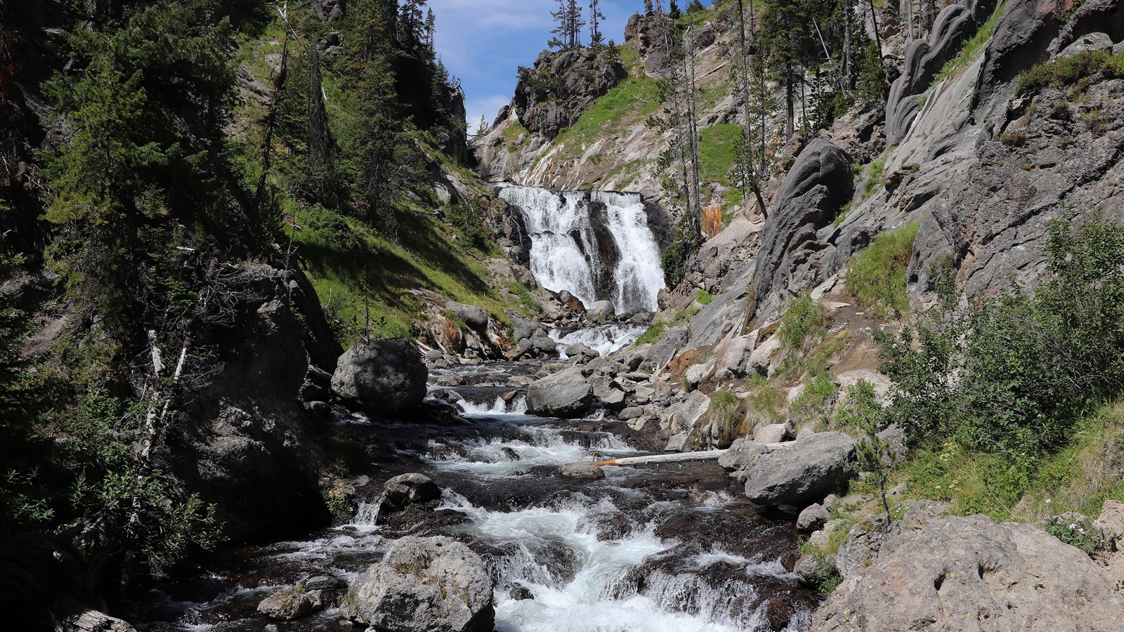 A waterfall cascades over a cliff and flows into a stream down a rocky creek.