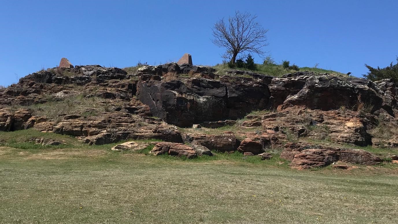 Sandstone outcropping with some grass in some places and a few tress and bushes on it.