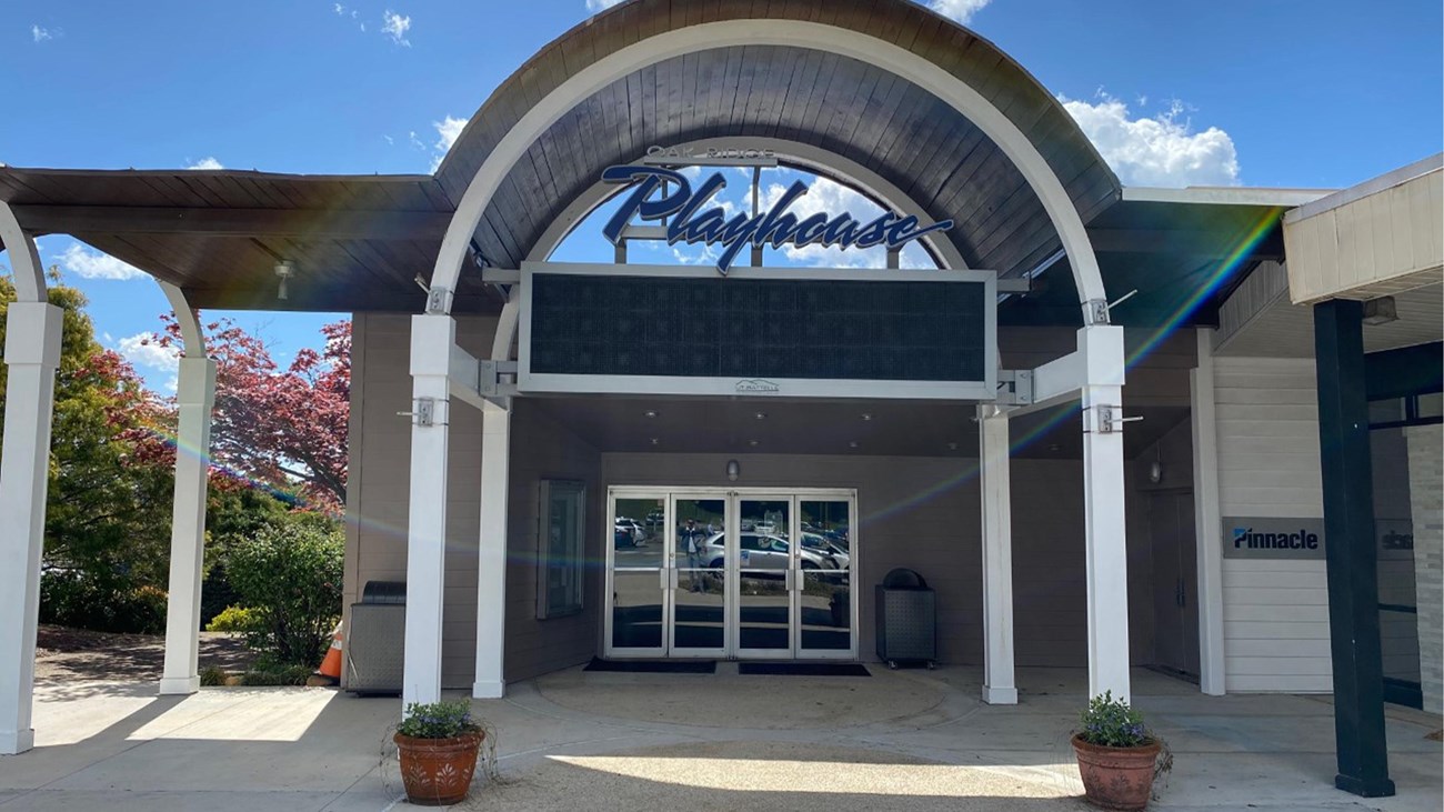 Exterior entrance to a theater with a curved roof that reads “Playhouse”. 