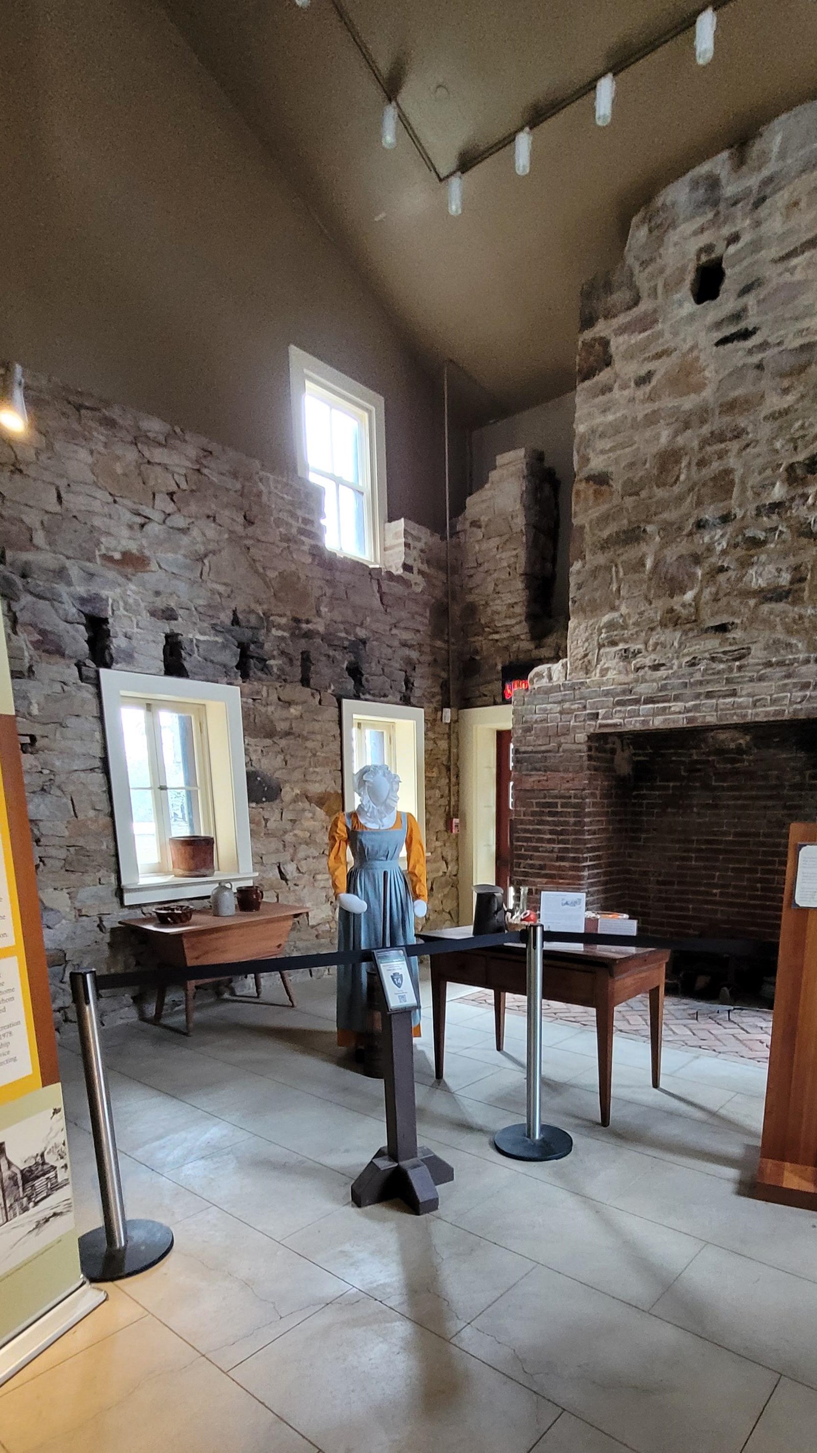 Stone room with kitchen tools and utensils. Banner of information on left, fireplace on right.