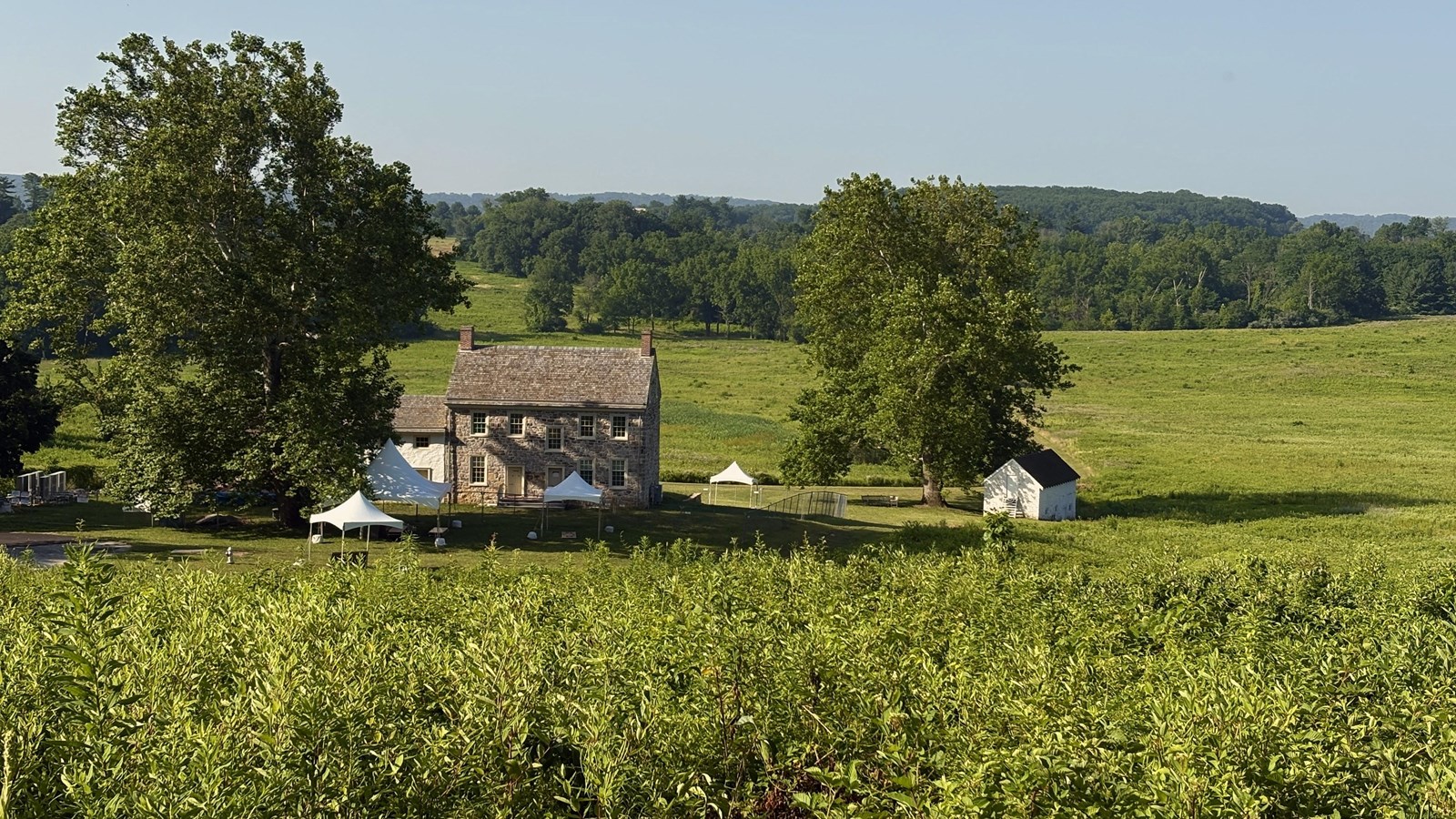 stone building, white topped tents, and a few trees in an expansive meadow