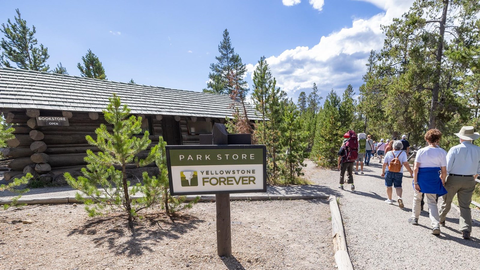 People walk along a gravel path next to a log cabin building.