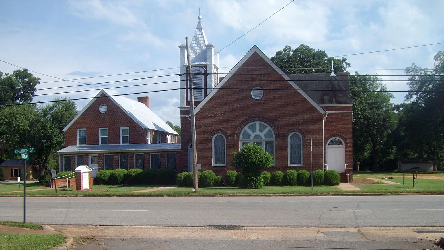 Plains United Methodist Church is a one story red brick building with a large stained glass window
