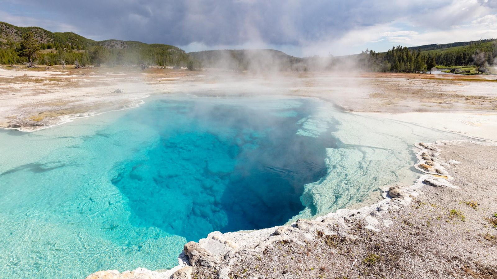 Steam rises off a deep, blue hot spring in a geyser basin.