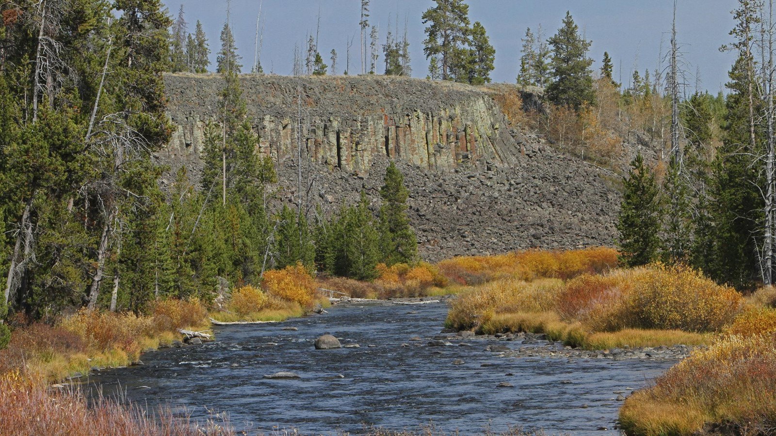 Columns of basalt erode into talus on a slope above a riverbank.