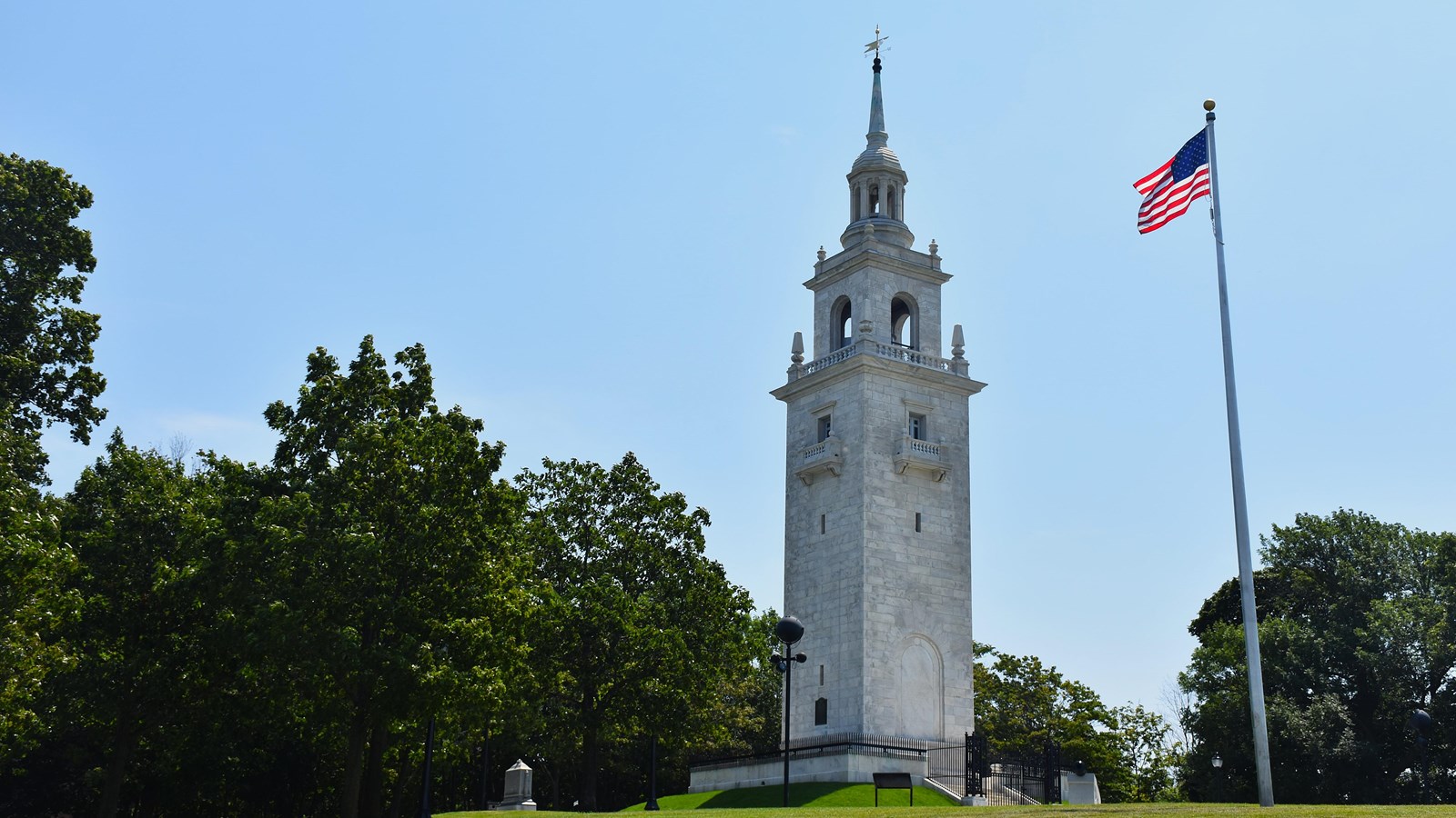 A tall white monument tower on a grassy area next to an American flag