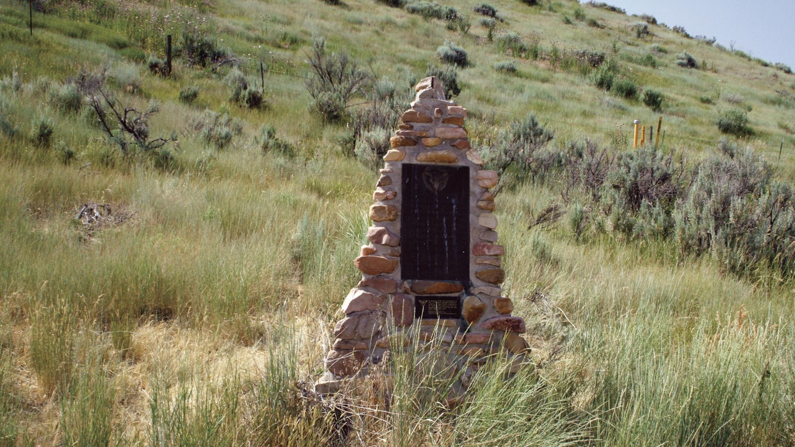 A stone monument sits on a grassy hill.