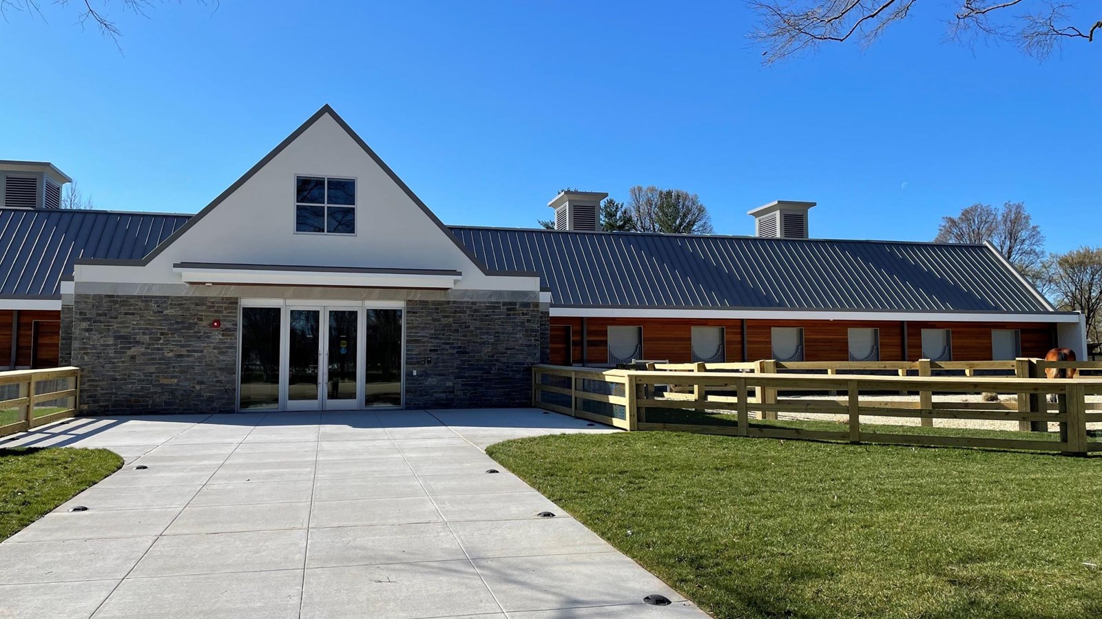 Long, one-story building with a triangular roof and a fenced-in paddock on the right