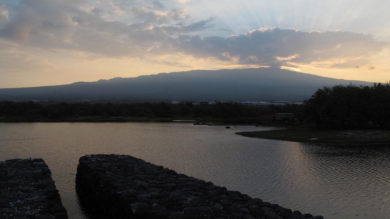 Makaha gate and fishpond wall with the sun rising over volcano in the background