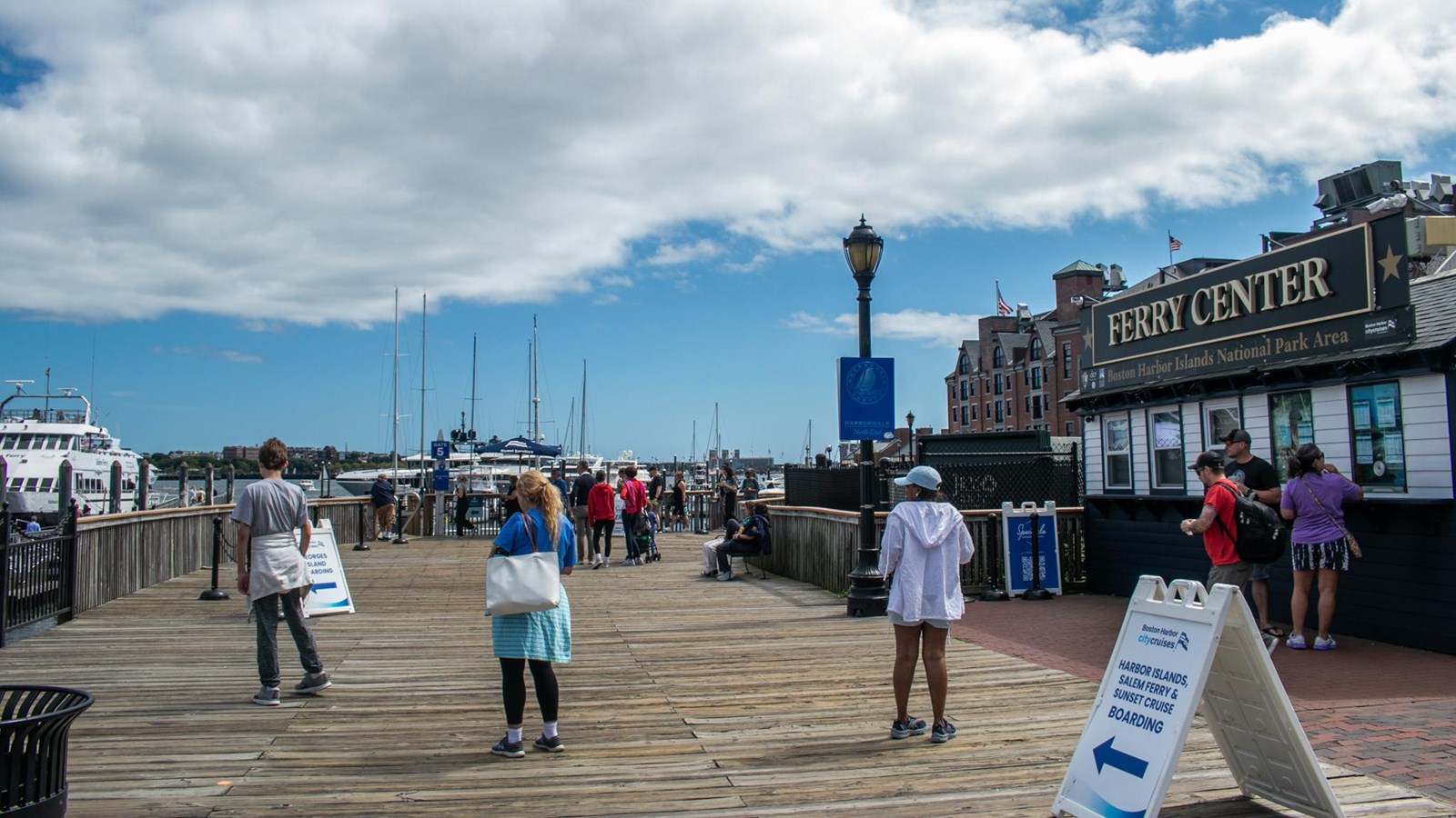 A building, the Ferry Center, welcomes visitors on the deck of the wharf, across from boats docked.