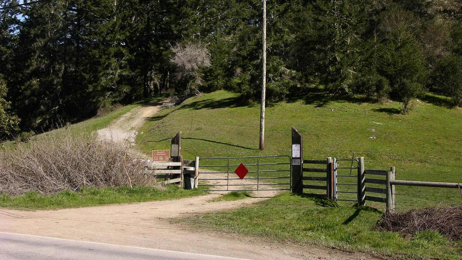 A wide trail passes through a gate and cattle pasture before heading up a forested hill.