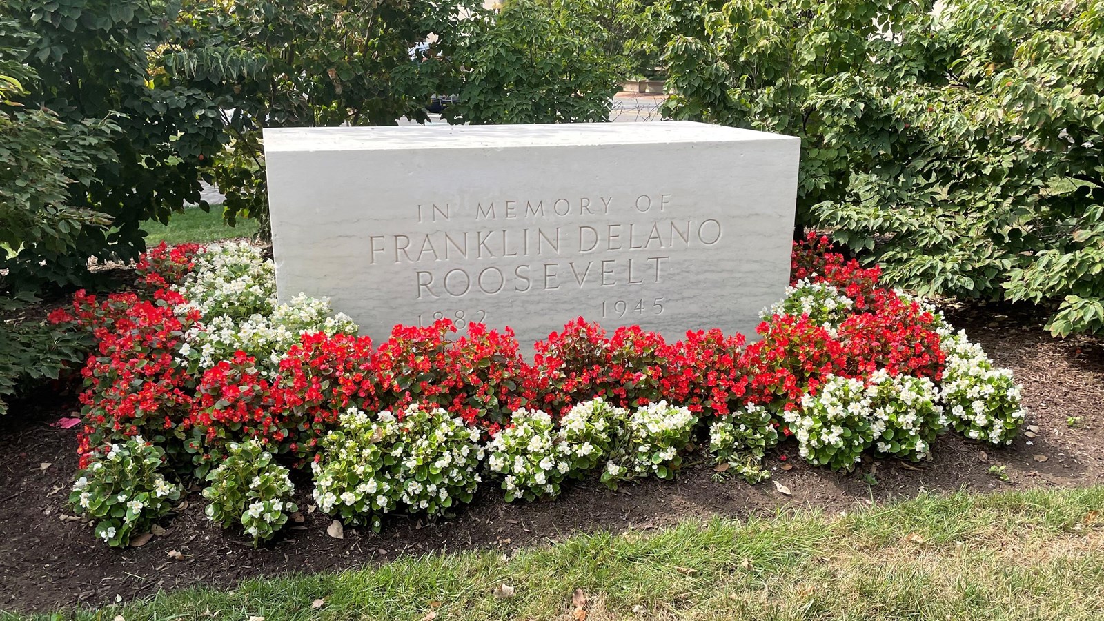 Large rectangular block of white marble with flowering shrubs at the base