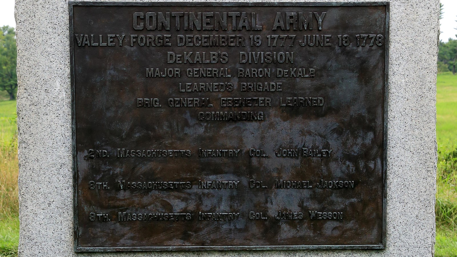 A large, smooth granite block with a bronze plaque. Sides and bottom are rough.