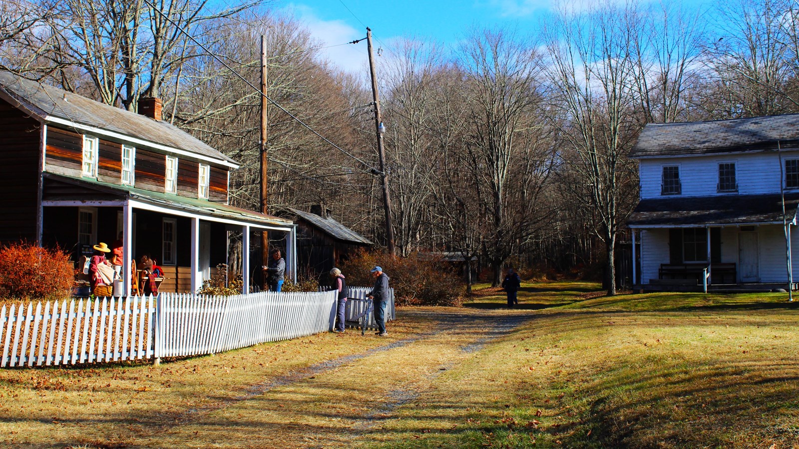 A brown two story building on the left with visitors and volunteers on the porch.