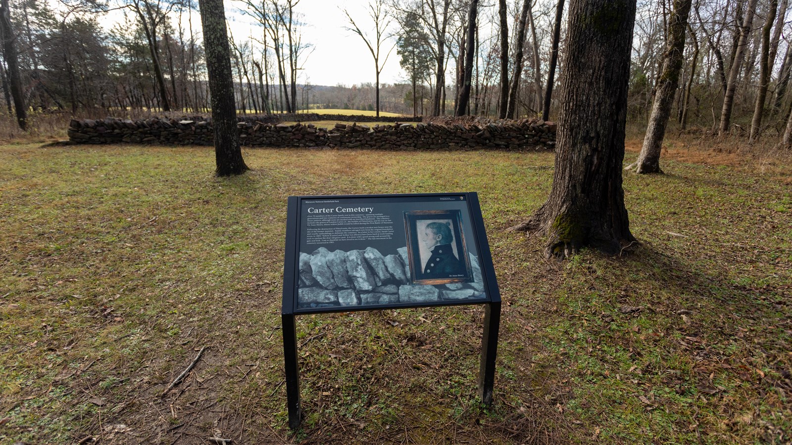 Stones stacked against each other are the background of a photo of a man wearing a buttoned jacket.