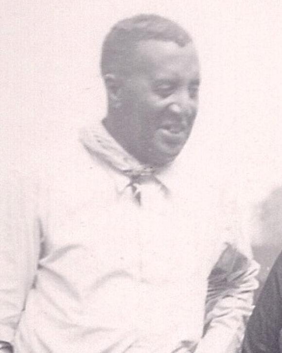 Candid black and white photo of a black man with white button down shirt & handkerchief around neck 